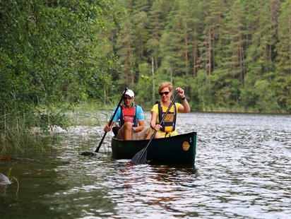 Kanutour im Nuuksio Nationalpark Zwei Menschen fahren Kanu auf einem Fluss in einem Nadelwald