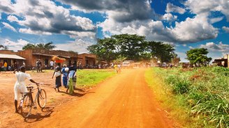 Straße durch eine Stadt in Uganda mit Fahrradfahrern an der Seite