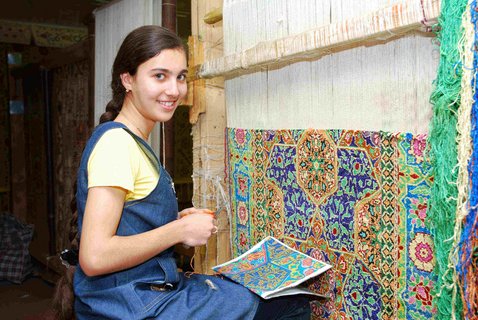Eine Frau knüpft nach einer Bildvorlage einen Teppich an der Wand