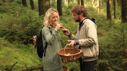 Ein Mann erläutert einer Frau einen im Wald gesammelten Pilz.
