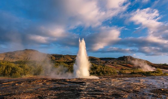 Ein sprudelnder Geysir umringt von Vulkangestein auf Island