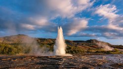 Ein sprudelnder Geysir umringt von Vulkangestein auf Island