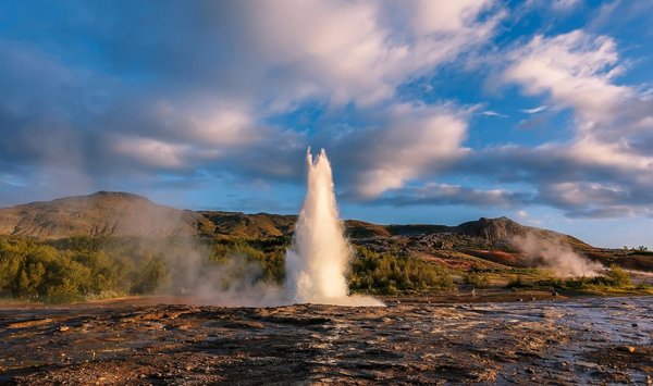 Ein sprudelnder Geysir umringt von Vulkangestein auf Island