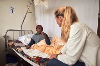 Eine westliche Ärztin besucht einen jungen einheimischen Patienten im Krankenzimmer des Africa Amini Alama-Projekts in Tansania.