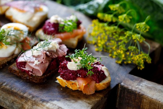 Das schwedische Smörgåsbord wartet mit einer Vielzahl an Speisevarianten auf Auf einem Holzbrett liegen mehrere unterschiedlich belegte Brotscheiben.