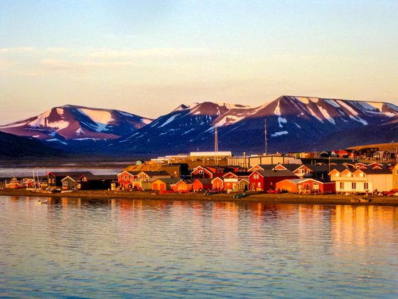 Mitternachtssonne an der norwegischen Longyearbyen-Küste Die warme Mitternachtssonne strahlt typisch rote Häuser an der Küste an