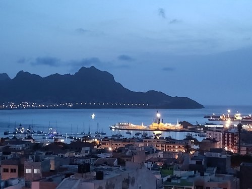 Man schaut über einige Häuser hinweg auf die Bucht Mindelos, die NAcht senkt sich.