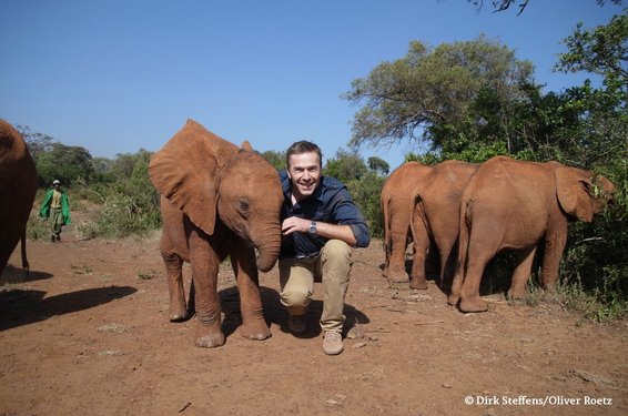 Dirk Steffens hockt neben einigen kleinen Elefanten in Afrika.