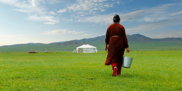 Ein mongolischer Bauer bringt einen Eimer Milch zu seiner Jurte