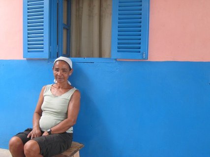Einheimische Frau der Kapverden sitzt auf einem Stuhl vor einer blau-rosa Hauswand