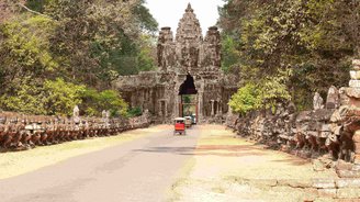 Tuk Tuks fahren auf einem Weg durch ein altes Steintor, auf dem man ein Buddha Gesicht erkennt