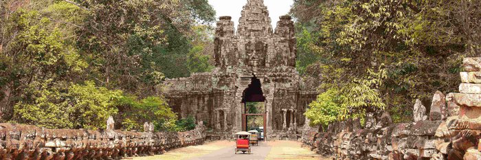 Tuk Tuks fahren auf einem Weg durch ein altes Steintor, auf dem man ein Buddha Gesicht erkennt