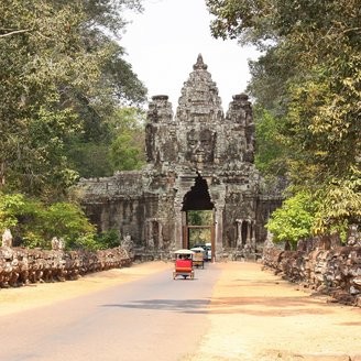 Tuk Tuks fahren auf einem Weg durch ein altes Steintor, auf dem man ein Buddha Gesicht erkennt