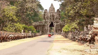 Angkor Thom entdecken: Unterwegs mit dem Tuk Tuk in Kambodscha Tuk Tuks fahren auf einem Weg durch ein altes Steintor, auf dem man ein Buddha Gesicht erkennt