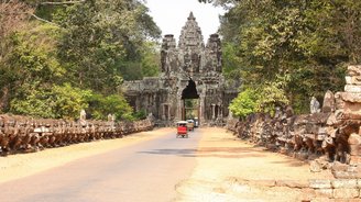 Tuk Tuks fahren auf einem Weg durch ein altes Steintor, auf dem man ein Buddha Gesicht erkennt