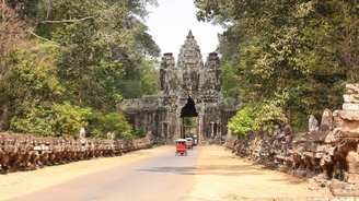 Tuk Tuks fahren auf einem Weg durch ein altes Steintor, auf dem man ein Buddha Gesicht erkennt
