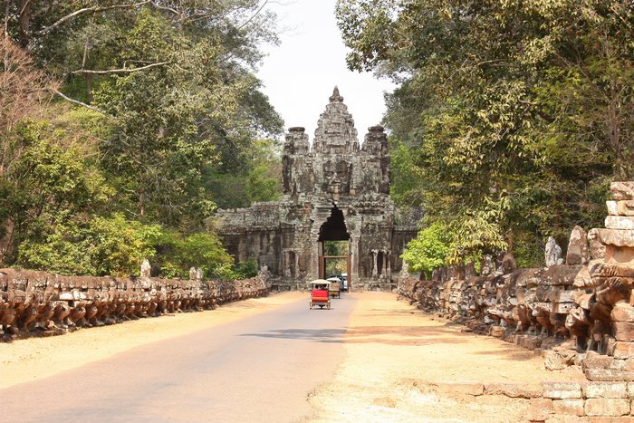 Tuk Tuks fahren auf einem Weg durch ein altes Steintor, auf dem man ein Buddha Gesicht erkennt