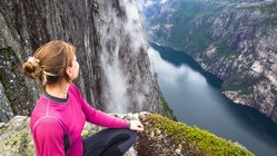 Wanderung in Kjerag, Norwegen Ein Wanderin sitzt hoch oben auf einem Berg und blick ins Tal auf einen blau schimmernden Fluss