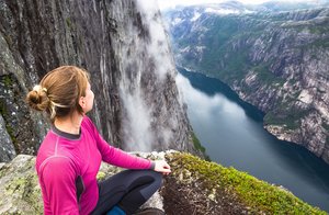 Wanderung in Kjerag, Norwegen Ein Wanderin sitzt hoch oben auf einem Berg und blick ins Tal auf einen blau schimmernden Fluss