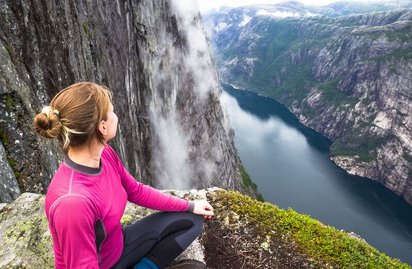 Wanderung in Kjerag, Norwegen Ein Wanderin sitzt hoch oben auf einem Berg und blick ins Tal auf einen blau schimmernden Fluss