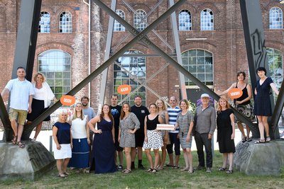 Das Reisen Mit Sinnen Team steht nebeneinander aufgestellt an einem Metallgestell vor einer Mauer.