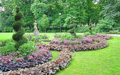 In einem Park sind auf einer Wiese Blumenrabatten angelegt. Dazwischen steht die Steinskulptur eines weiblichen Torsos.