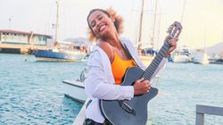 Frau spielt Gitarre am Wasser. 