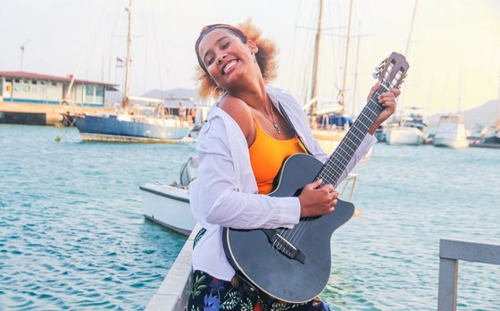 Frau spielt Gitarre am Wasser. 