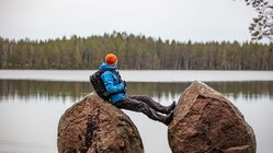 Ein Mann lehnt sich an einen großen Stein und blickt auf einen See