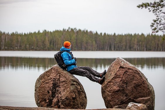 Ein Mann lehnt sich an einen großen Stein und blickt auf einen See