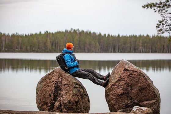 Ein Wanderer entspannt an einem See im Nuuksio Nationalpark Ein Mann lehnt sich an einen großen Stein und blickt auf einen See