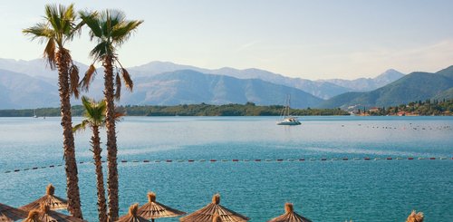 Sonnenschirme, Palmen und der Ausblick aufs Meer an der Adriaküste in Montenegro.