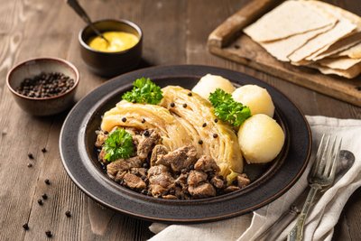 Auf einem irdenen Teller liegt zerkleinertes Lammfleisch mit Kohlspalten und Klößen.