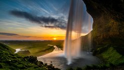 Vor einem Sonnenuntergang sieht man seitwärts auf den hintergehbaren Seljalandsfoss-Wasserfall auf Island.