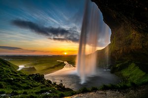 Vor einem Sonnenuntergang sieht man seitwärts auf den hintergehbaren Seljalandsfoss-Wasserfall auf Island.