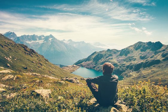 Atemberaubender Ausblick auf eine Seelandschaft Wanderer sitzt oben in den Bergen und blickt auf eine Seelandschaft