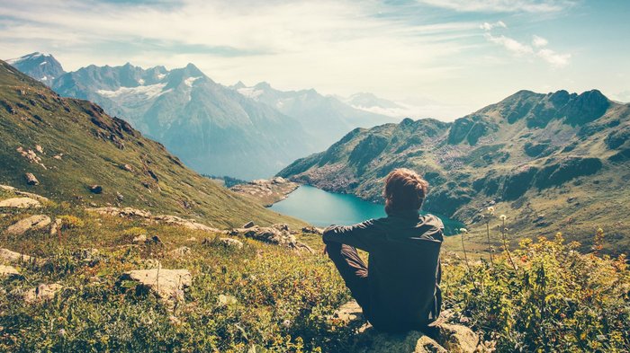 Wanderer sitzt oben in den Bergen und blickt auf eine Seelandschaft