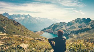 Wanderer sitzt oben in den Bergen und blickt auf eine Seelandschaft