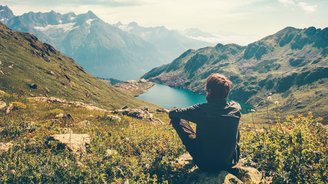 Wanderer sitzt oben in den Bergen und blickt auf eine Seelandschaft