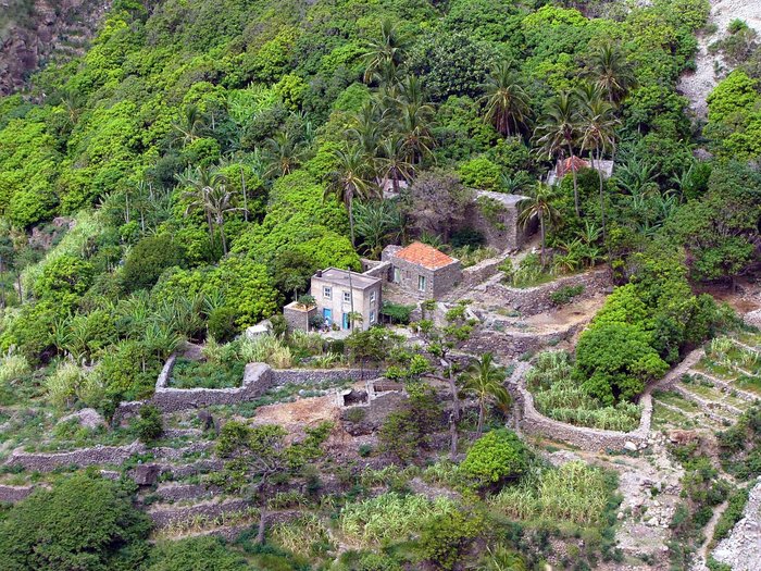 Steinhaus mit Steinmauern an einem Hügel, umgeben von grüner, üppiger Vegetation.