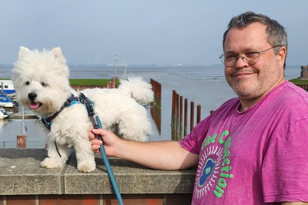 Reiseberater Dominik Mohr am Wasser mit seinem weißen kleinen Hund an der Leine.