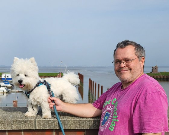 Reiseberater Dominik Mohr am Wasser mit seinem weißen kleinen Hund an der Leine.