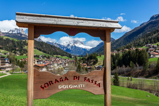 Ortseingang von Soraga di Fassa Durch ein hölzernes Ortseingangsschild blickt man auf die Ortschaft Soraga im Fassa-Tal.