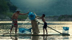 Vater und Sohn holen auf einem Floß den Fischfang ein