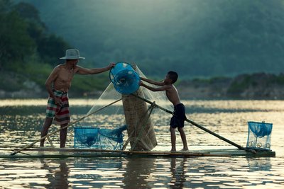 Fischen auf dem Fluss in Laos Vater und Sohn holen auf einem Floß den Fischfang ein