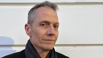 Portrait eines Mannes mit grauen Haaren, schwarzer Jacke und schwarzem Schal.