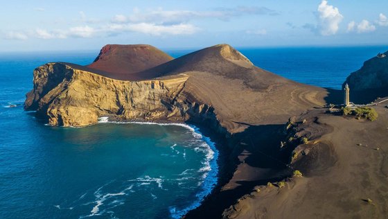 In das Meer hinein ragt eine Landzunge aus grauem Lavagestein.