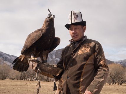 Auf dem Arm eines Kirgisen in traditioneller Jägerkluft sitzt ein Adler