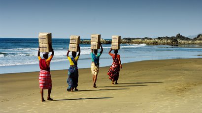 Frauen in traditioneller Kleidung am Strand tragen Kisten auf ihren Köpfen 