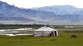 Familie steht vor einer Jurte in einer Wiesen Landschaft
